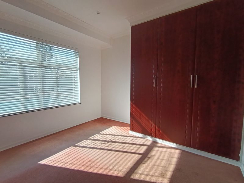 A bright, empty bedroom featuring built-in wooden cupboards, venetian blinds, and decorative cornice detailing.