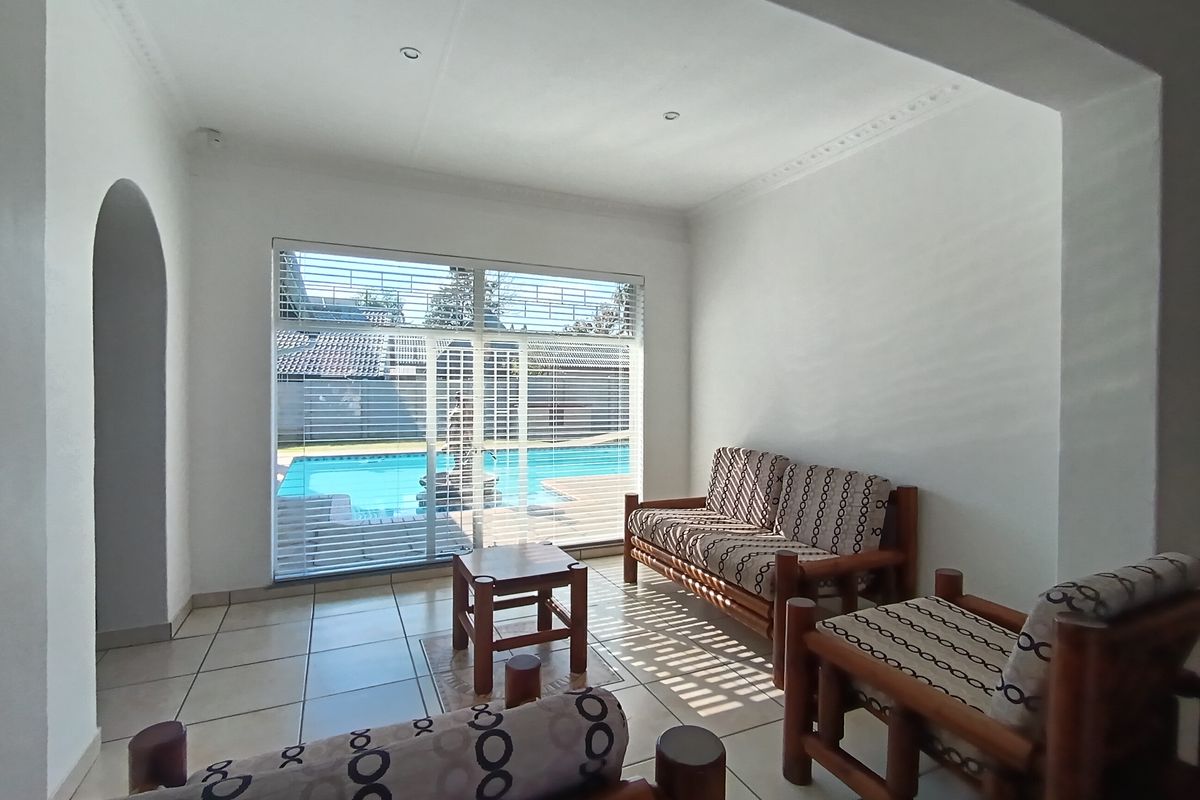 A bright living room featuring tiled flooring, recessed lighting, and a large sliding glass door providing direct access and views to the outdoor pool area.