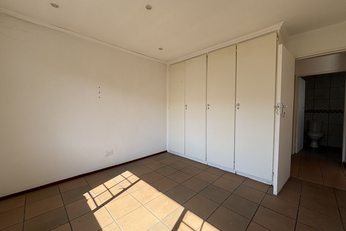 An empty bedroom featuring tiled flooring, built-in cupboards, and recessed downlights, with an adjacent view into a bathroom.
