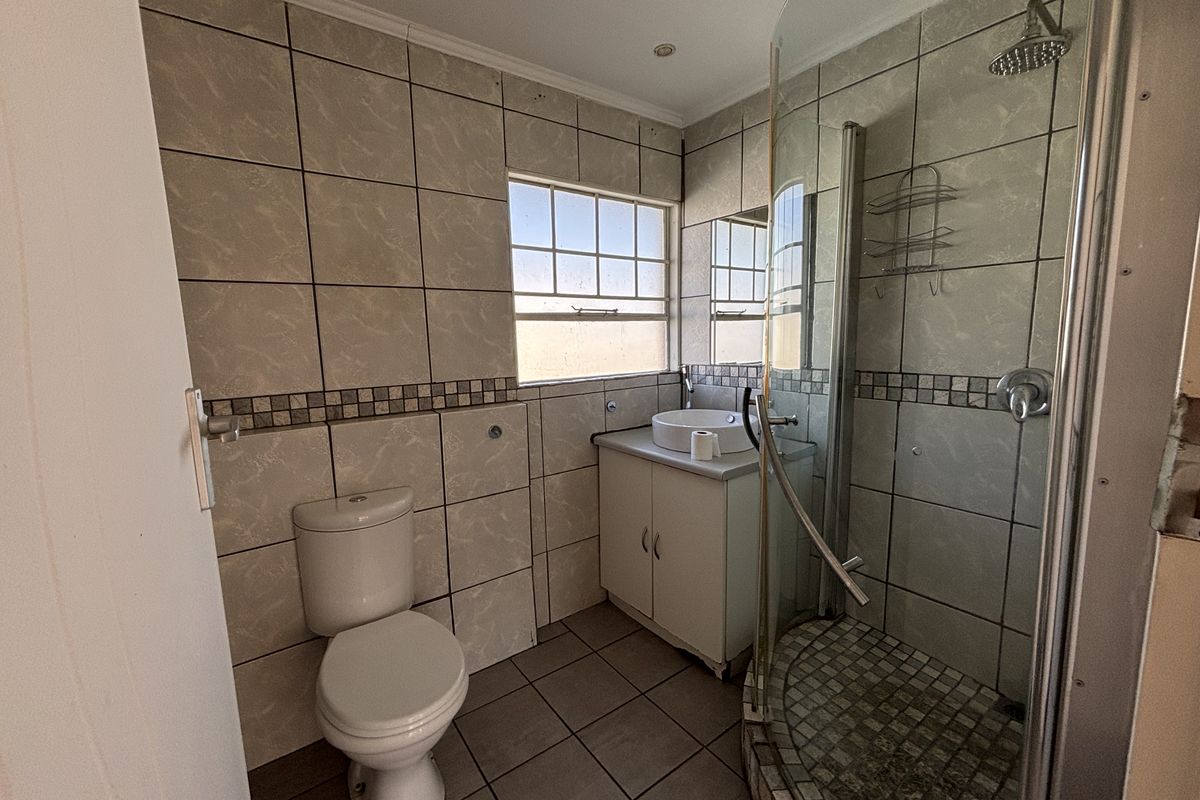 A functional bathroom featuring a corner shower enclosure, vanity basin, and toilet with neutral wall and floor tiling.