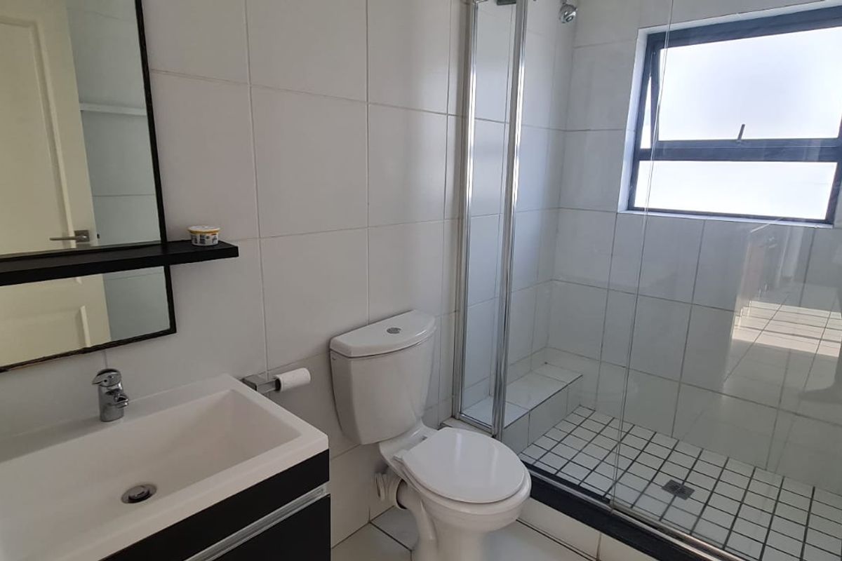 A modern bathroom featuring a vanity with basin, a toilet, and a walk-in shower with a glass enclosure and tiled flooring.