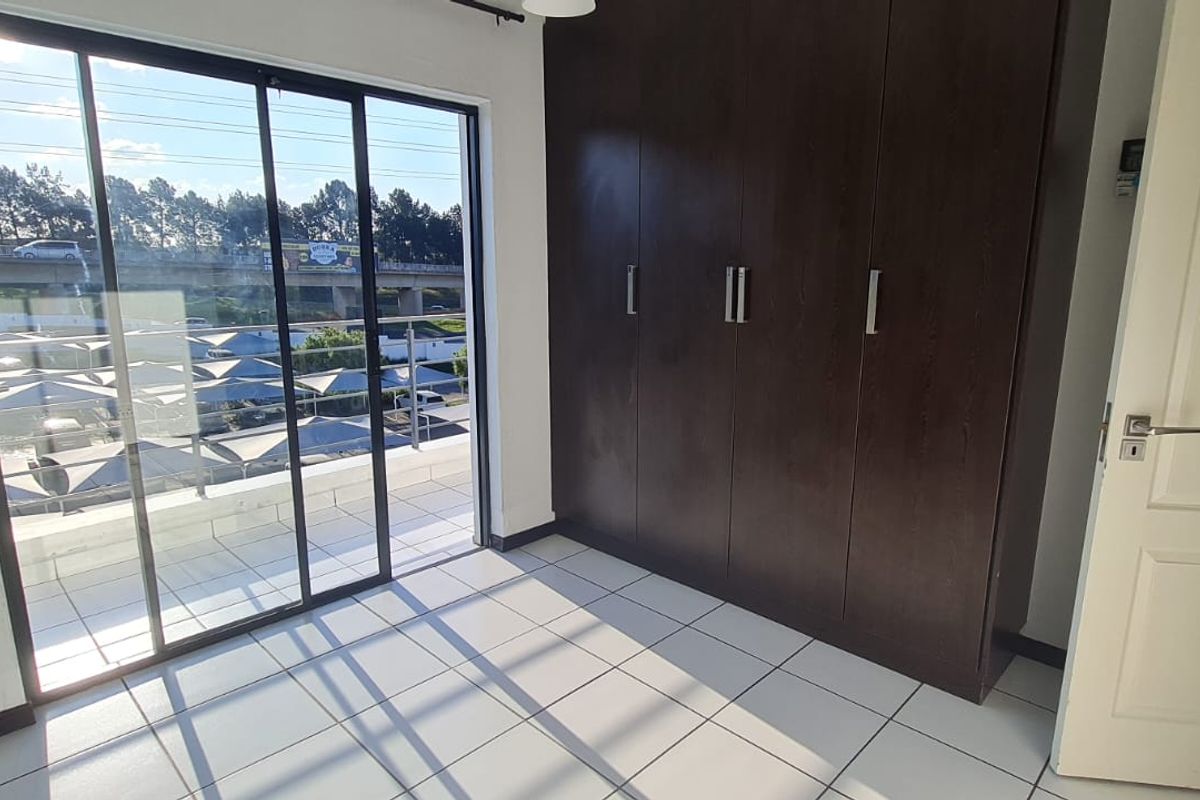 A bright, empty bedroom featuring tiled flooring, dark wood built-in cupboards, and a sliding glass door leading to an outdoor balcony.