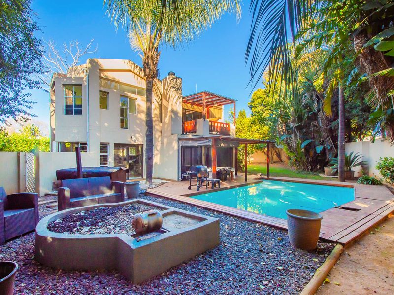 Rear exterior view featuring a swimming pool, timber decking, built-in fire pit, and a covered patio area with balcony access.