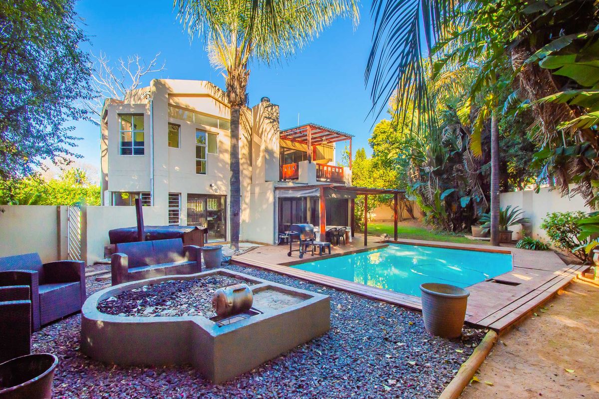 Rear exterior view featuring a swimming pool, timber decking, built-in fire pit, and a covered patio area with balcony access.