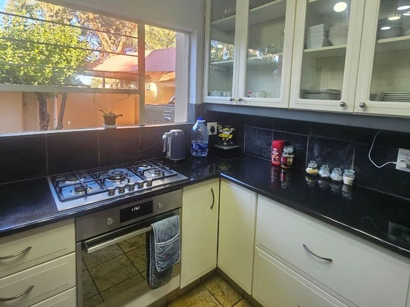 A functional kitchen featuring white cabinetry, black granite countertops, a built-in gas hob, and an oven, with a window overlooking the exterior.