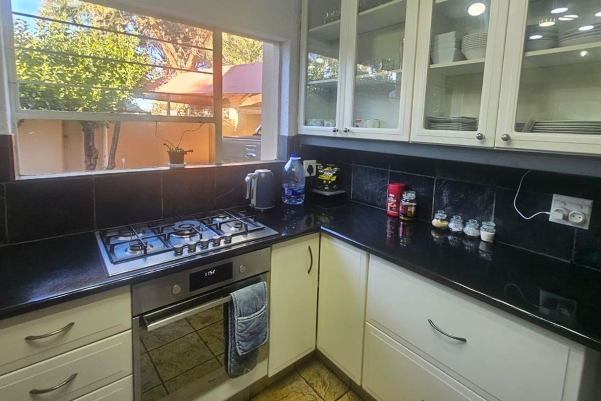 A functional kitchen featuring white cabinetry, black granite countertops, a built-in gas hob, and an oven, with a window overlooking the exterior.