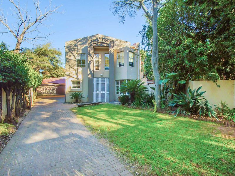 Front view of a two-story residential property featuring a paved driveway, established garden, and secure entrance gate.