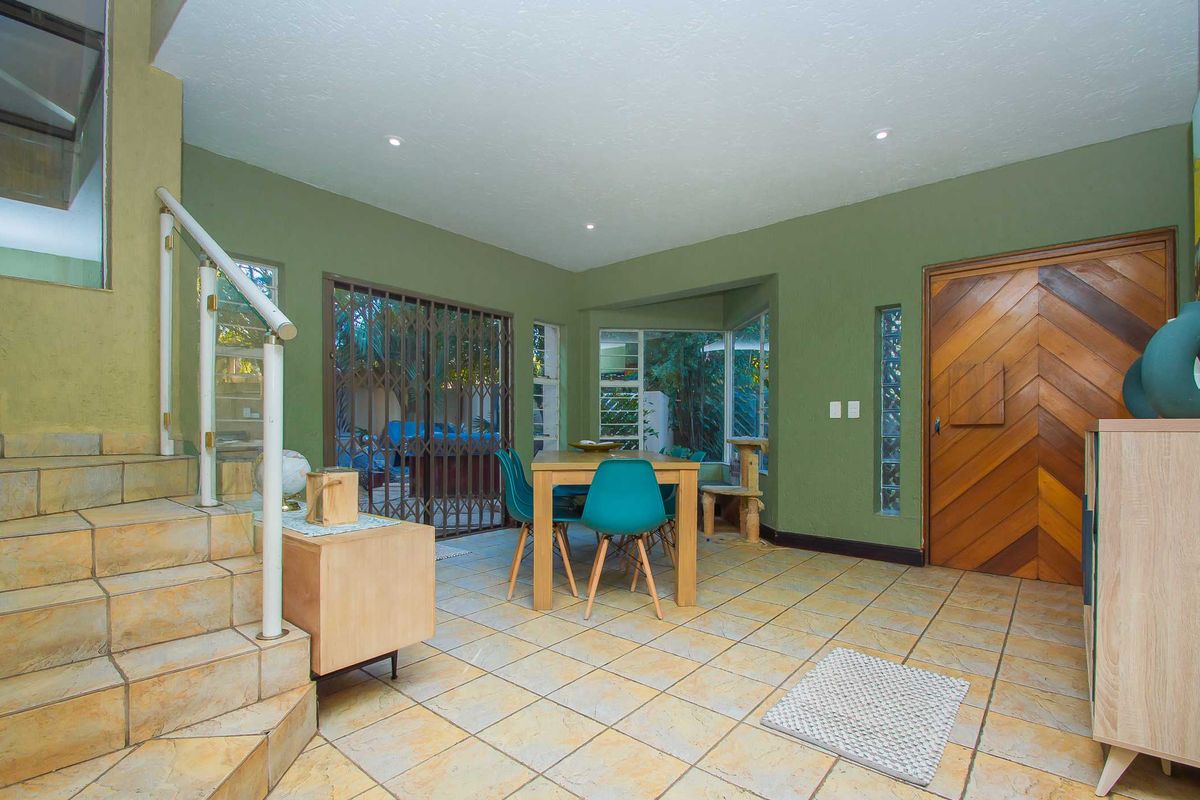 Open plan living area featuring tiled flooring, a staircase with metal railing, a unique glass block window, and a decorative wooden entrance door.