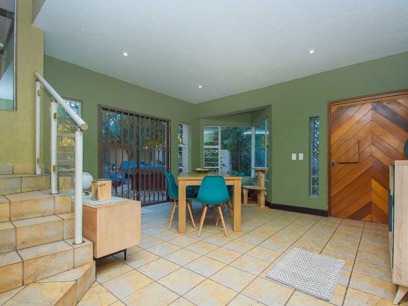 Open plan living area featuring tiled flooring, a staircase with metal railing, a unique glass block window, and a decorative wooden entrance door.