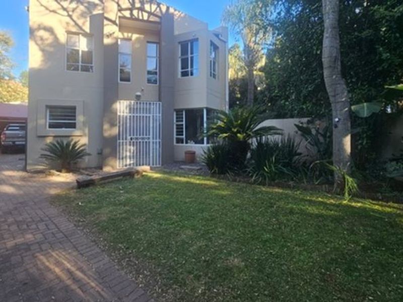 Front view of a double-storey house featuring a paved driveway, security gate entrance, and established garden area.