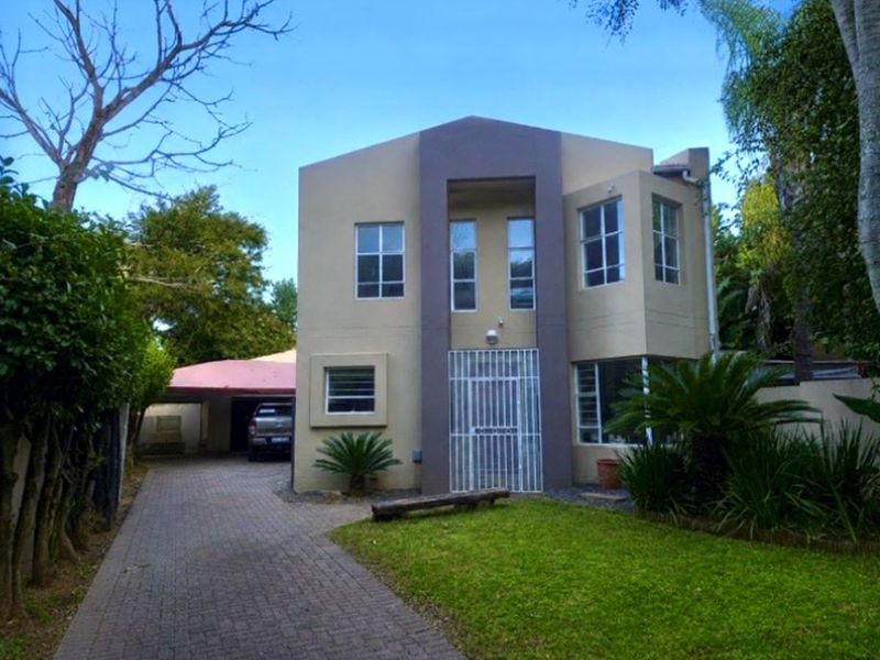 Front elevation of a two-story residential property featuring a paved driveway, attached carport, and established garden area.
