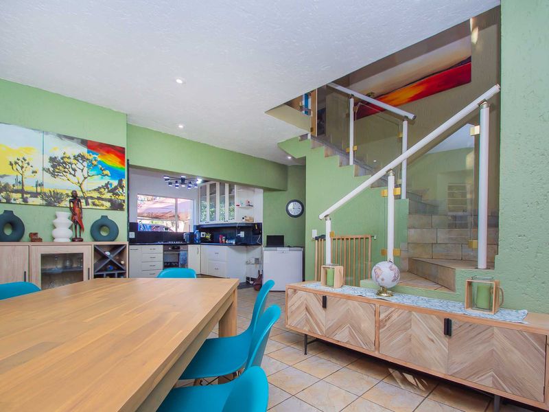 Open-plan living and dining area featuring a staircase with glass balustrade and a functional kitchen with built-in cabinetry and integrated appliances.