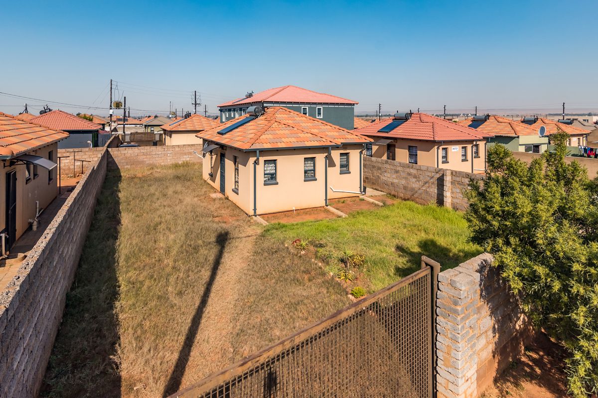 An aerial view of a residential property featuring a tiled roof, solar geyser, and a fenced backyard with a lawn.
