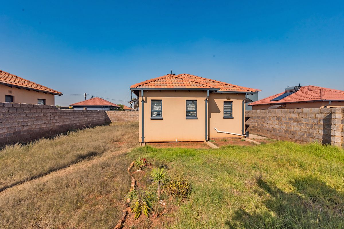 Rear view of a detached house featuring a tiled roof, exterior walls, and a large surrounding yard enclosed by brick boundary walls.