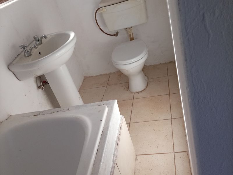 A functional bathroom featuring a pedestal basin, toilet, and bathtub with tiled flooring, requiring cosmetic updates to improve its overall condition.