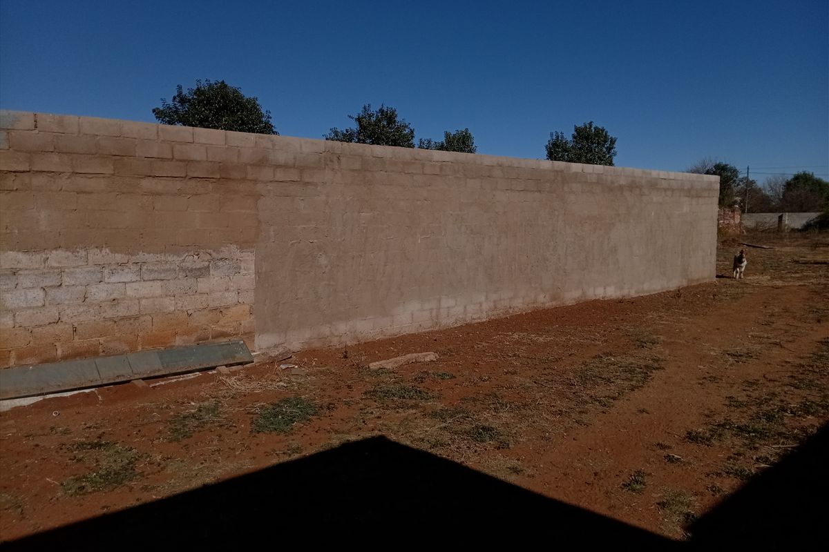 A view of a large, unfinished concrete block boundary wall in the rear yard area.