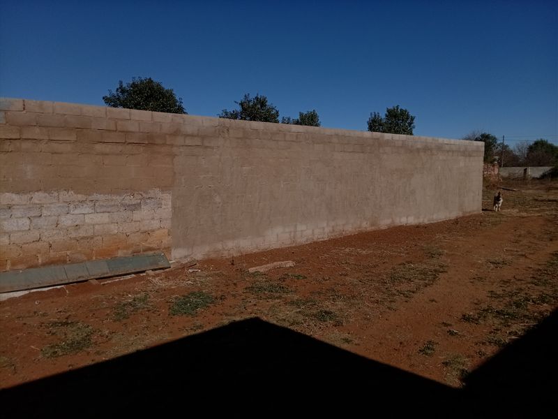 A view of a large, unfinished concrete block boundary wall in the rear yard area.
