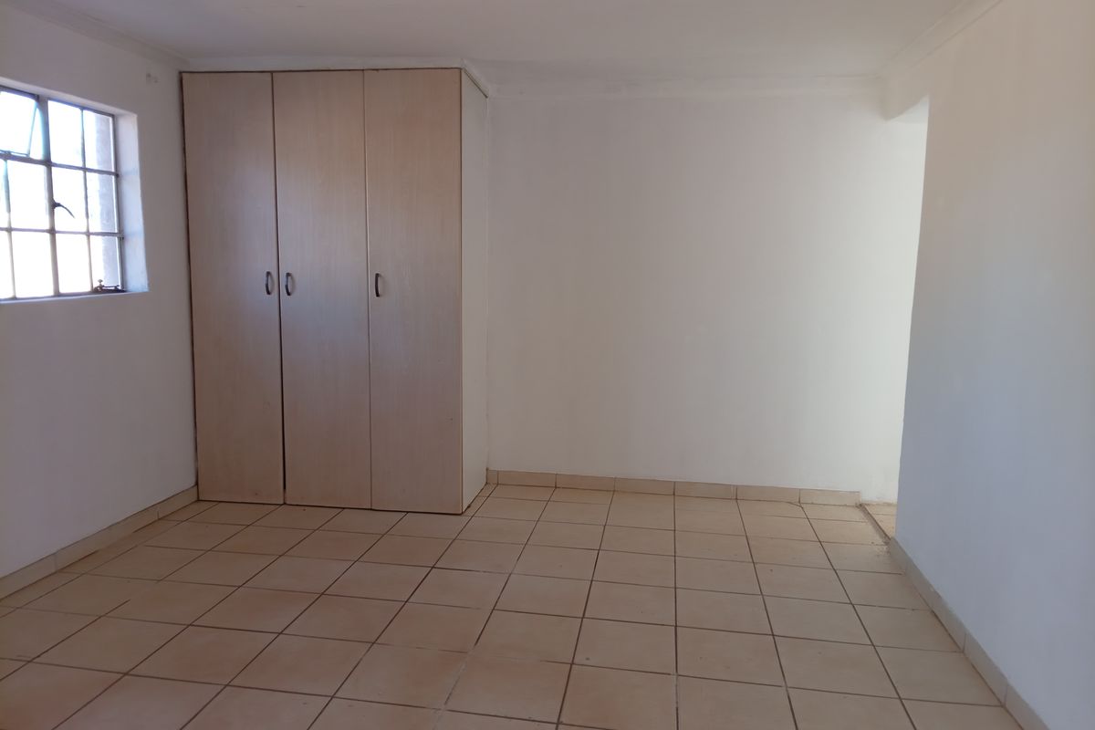 A clean, empty bedroom featuring neutral tiled flooring, a built-in wardrobe, and a steel-framed window, offering a blank canvas for personalization.