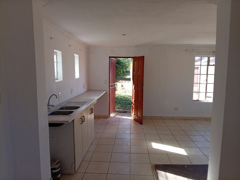 An empty kitchen area featuring tiled flooring, built-in base cabinetry with a double sink, and direct access to the exterior via a security gate.