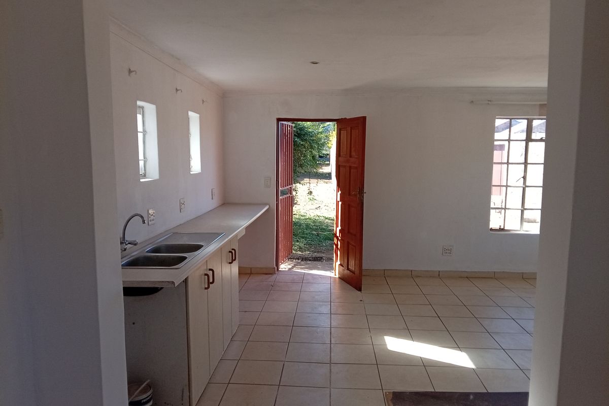 An empty kitchen area featuring tiled flooring, built-in base cabinetry with a double sink, and direct access to the exterior via a security gate.