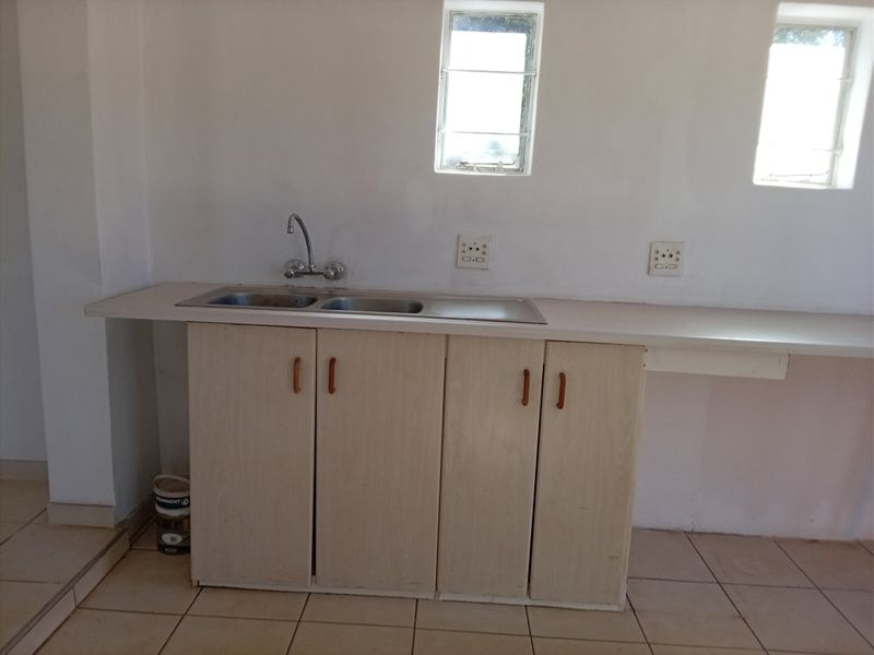 A basic, empty kitchen area featuring a stainless steel sink, laminate cabinetry, and tiled flooring, ready for renovation or modernization.