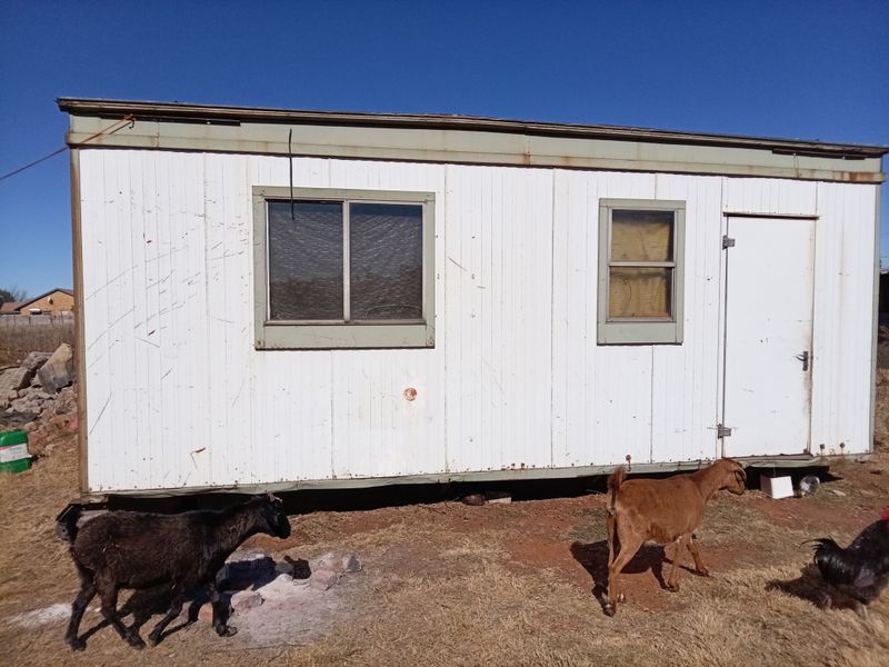A view of a portable cabin structure with metal siding and windows, situated on a vacant residential lot.