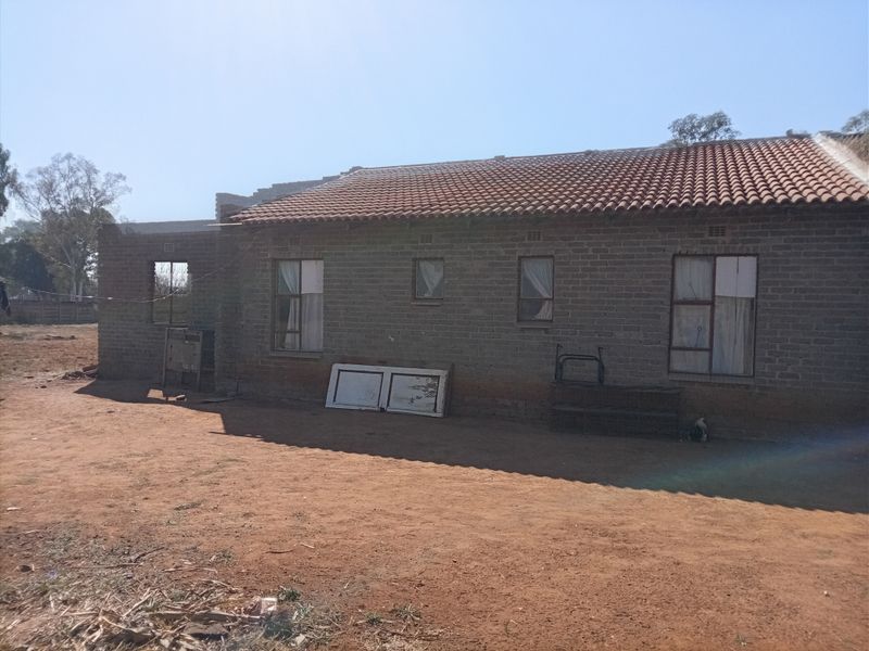 Rear view of a single-story house featuring exposed brick construction, terracotta roof tiles, and steel-framed windows, currently in an unfinished state.