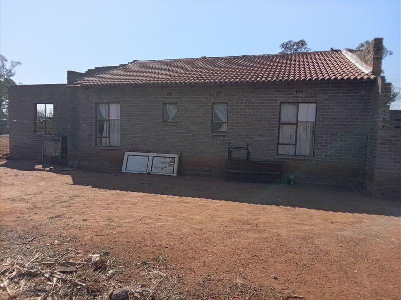 Rear view of a single-story house featuring exposed brick walls, terracotta roof tiles, and steel-framed windows, currently in an unfinished state.
