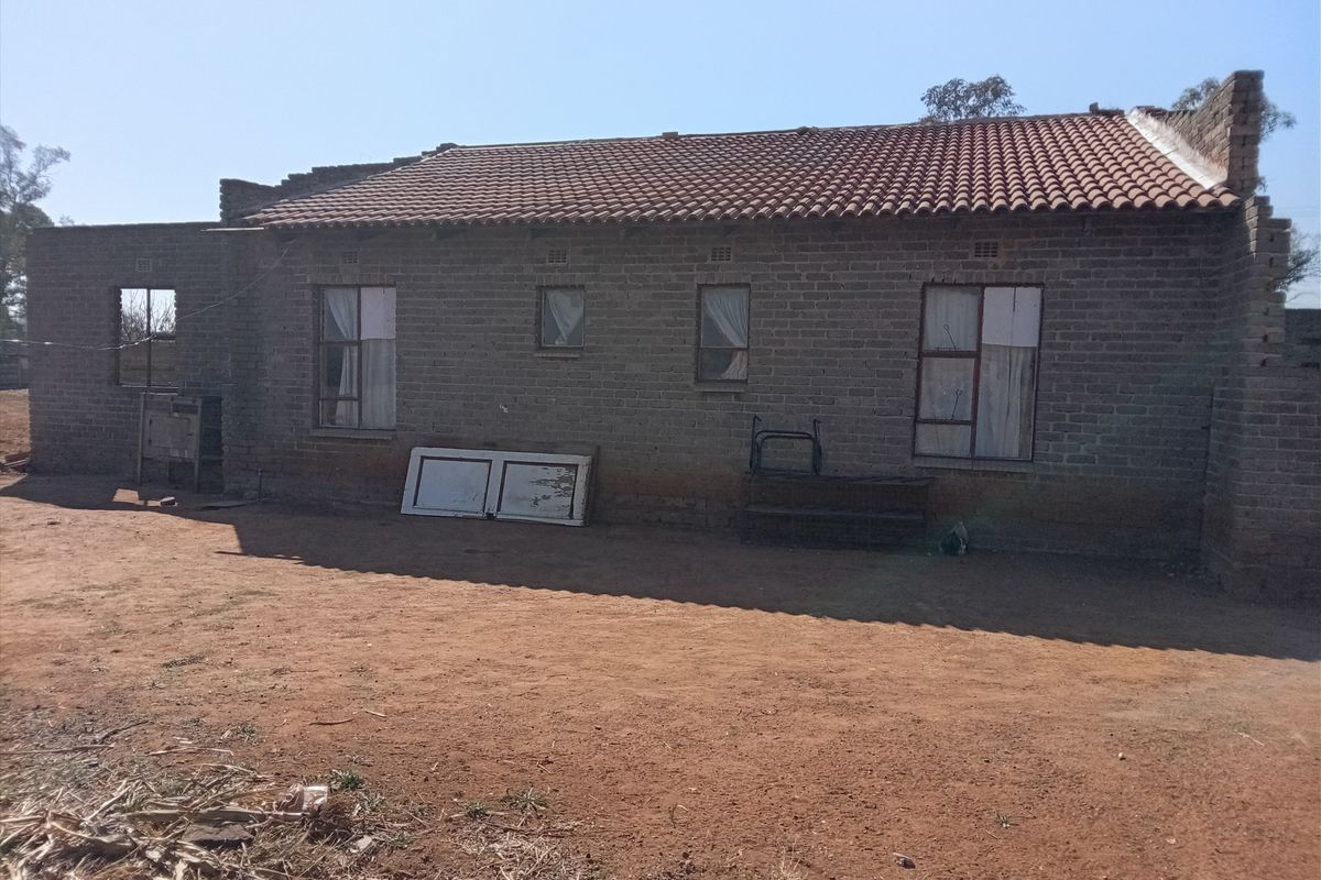 Rear view of a single-story house featuring exposed brick walls, terracotta roof tiles, and steel-framed windows, currently in an unfinished state.