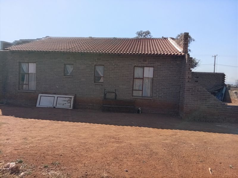 Rear view of a single-story brick house featuring a terracotta tiled roof and unfinished masonry work on the side elevation.