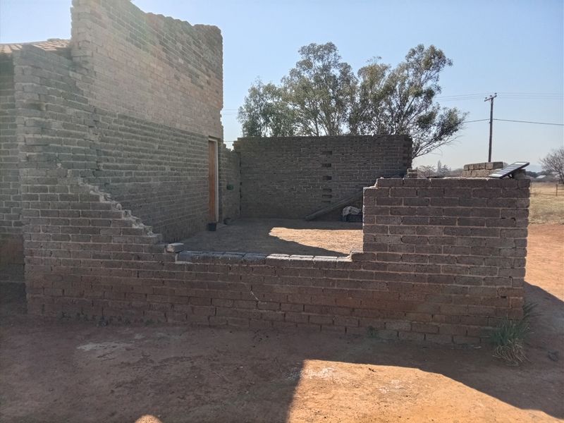 An unfinished brick structure showing exposed masonry walls and an open layout, currently lacking a roof and complete wall enclosures.