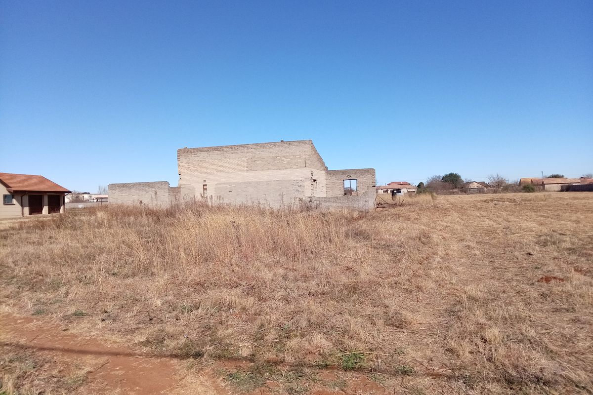 An unfinished concrete block structure set on a large, undeveloped plot of land, showing the early stages of residential construction.