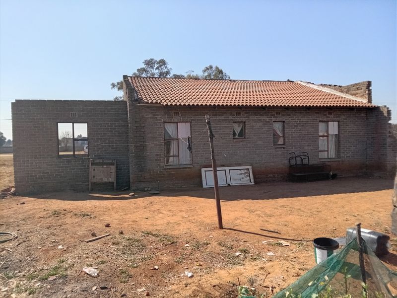 Rear view of a single-story brick house showing unfinished construction, exposed brick walls, and missing roof sections.