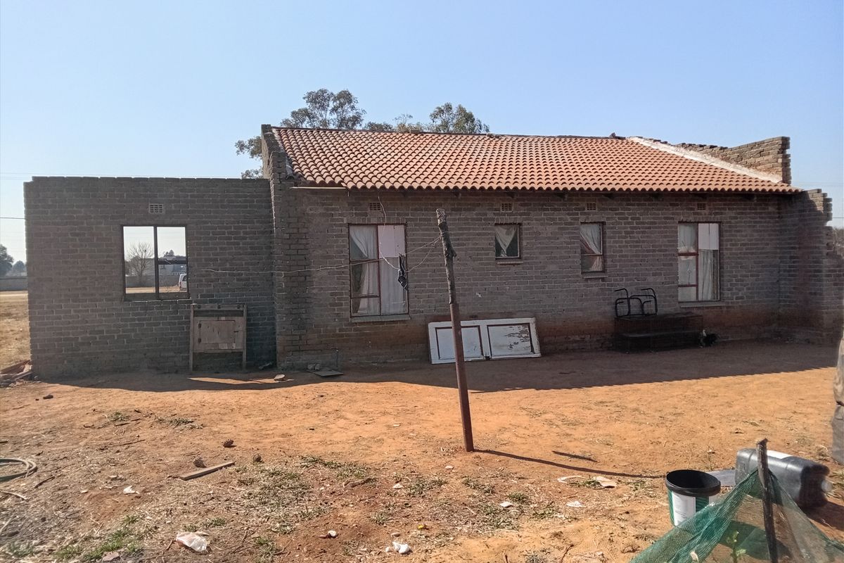 Rear view of a single-story brick house showing unfinished construction, exposed brick walls, and missing roof sections.