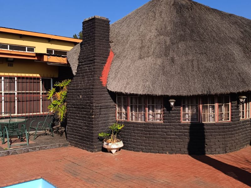 Outdoor pool area featuring a traditional thatched roof structure with a brick chimney and paved patio space.