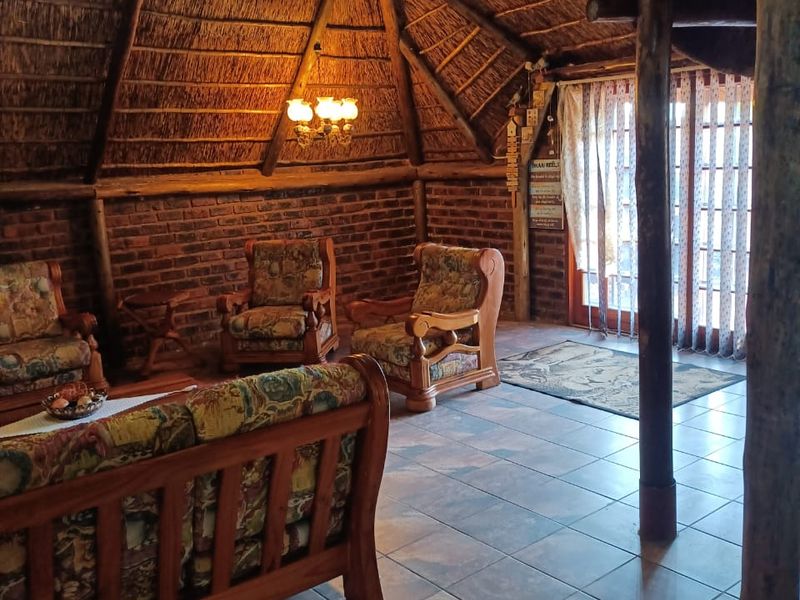 A rustic living room featuring a high thatched ceiling with exposed timber rafters, exposed brick walls, and ceramic tiled flooring.