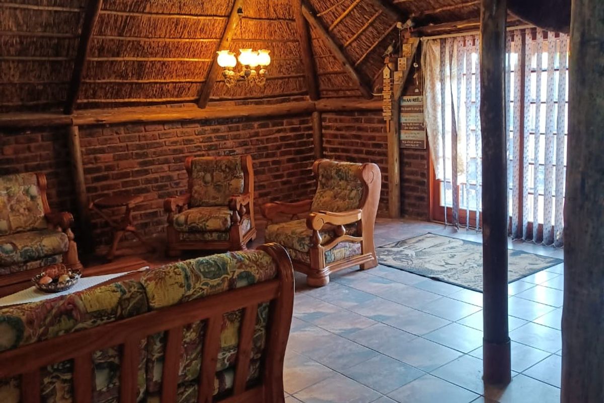 A rustic living room featuring a high thatched ceiling with exposed timber rafters, exposed brick walls, and ceramic tiled flooring.