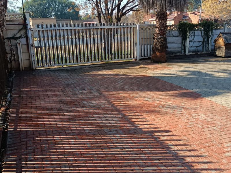 A paved front driveway area featuring a secure metal gate, perimeter walling, and established garden landscaping.