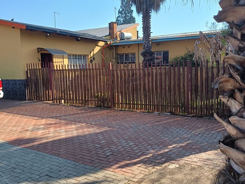 Front exterior view of the house featuring a paved driveway, metal picket fencing, and a solar water heater mounted on the roof.