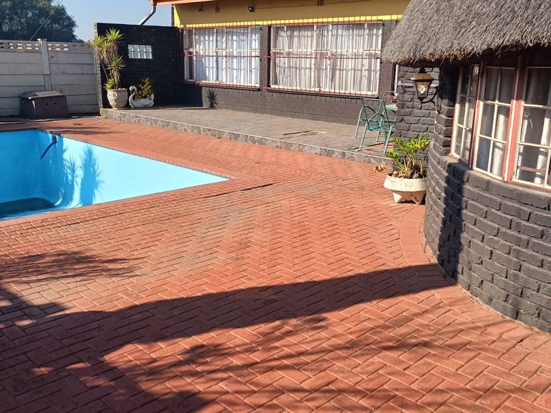 Outdoor pool area featuring brick paving, a thatched roof structure, and perimeter security walling.