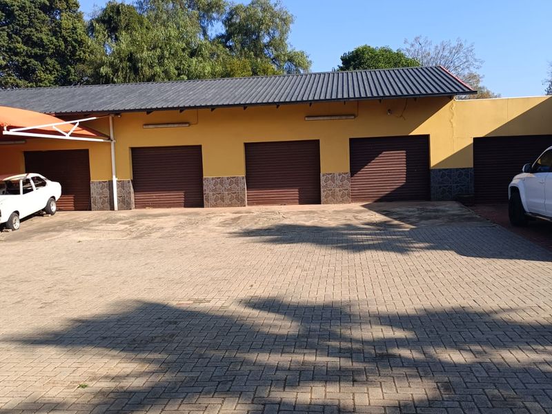 A multi-bay garage facility featuring roller shutter doors, a metal roof, and a spacious paved driveway area.