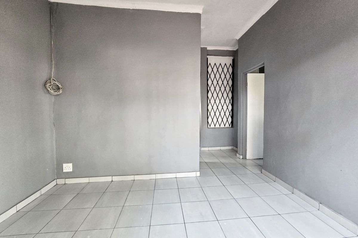 An empty living area featuring grey painted walls, ceramic floor tiles, and a security gate on the window.