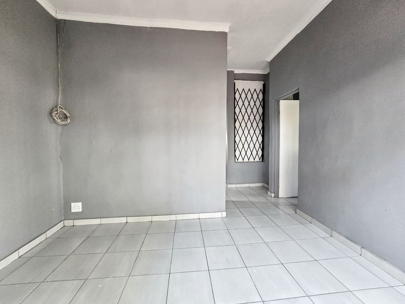 An empty living area featuring grey painted walls, ceramic floor tiles, and a security gate on the window.