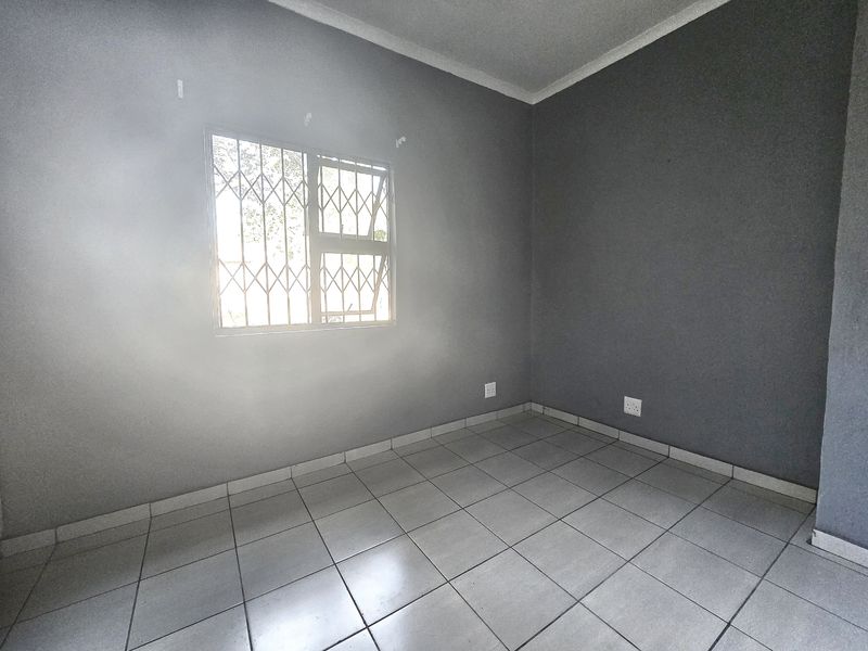 A vacant bedroom featuring neutral grey walls, tiled flooring, and a window fitted with a security gate.
