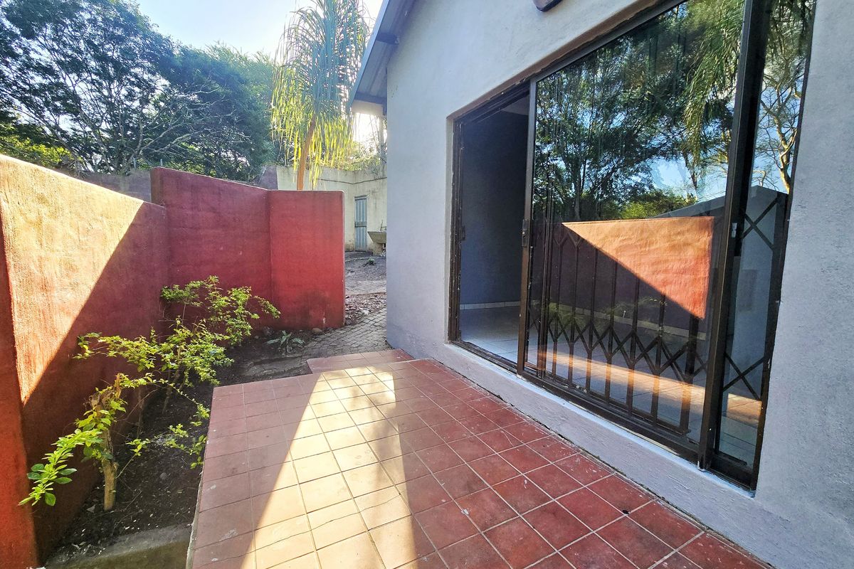 Rear exterior view of the cottage featuring a tiled patio area, sliding glass doors with security gate, and a private boundary wall.