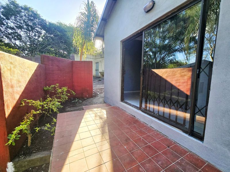 Rear exterior view of the cottage featuring a tiled patio area, sliding glass doors with security gate, and a private boundary wall.