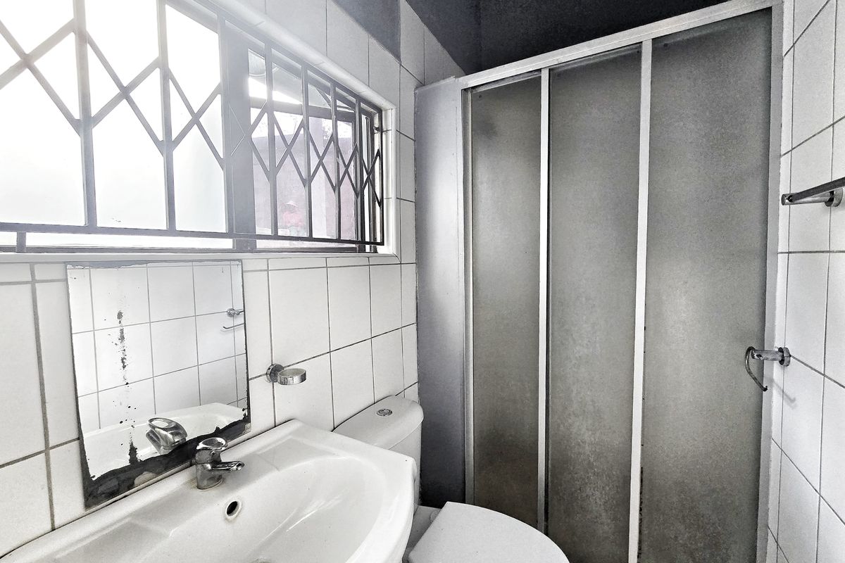 A functional bathroom featuring a pedestal basin, toilet, and shower enclosure with tiled walls and a security gate on the window.