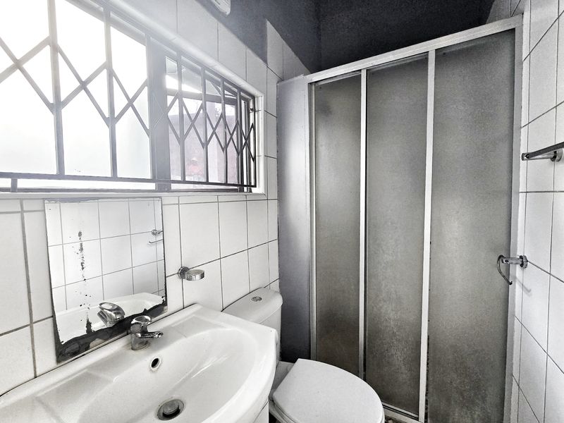 A functional bathroom featuring a pedestal basin, toilet, and shower enclosure with tiled walls and a security gate on the window.