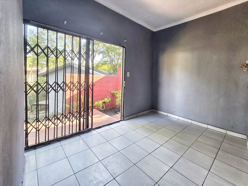 An empty living room featuring tiled flooring, coved ceilings, and a sliding glass door with a security gate leading to the rear garden.