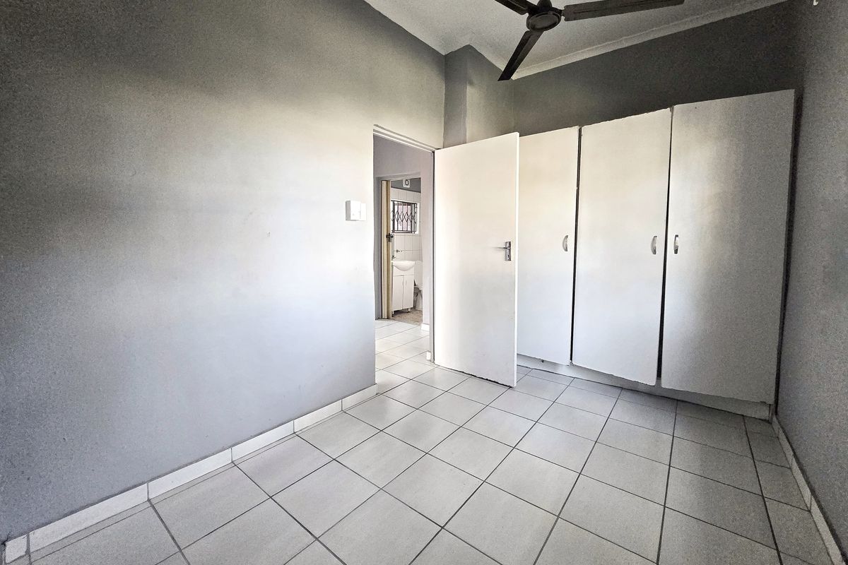 A vacant bedroom featuring tiled flooring, built-in cupboards, and a ceiling fan, with direct access to an adjoining bathroom.